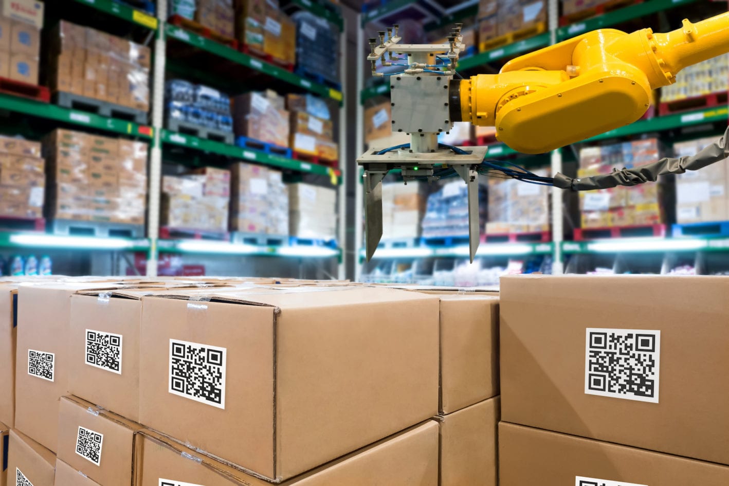 A digital manufacturing warehouse image with a robotic machine and cardboard boxes with QR codes.